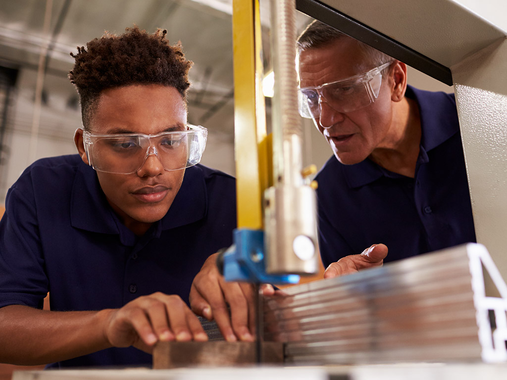 Carpenter Training Male Apprentice To Use Mechanized Saw